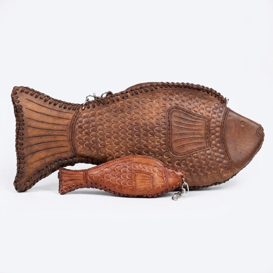 A large dark tan leather fish bag lying flat, with a smaller reddish leather fish coin purse resting on top of it for scale.