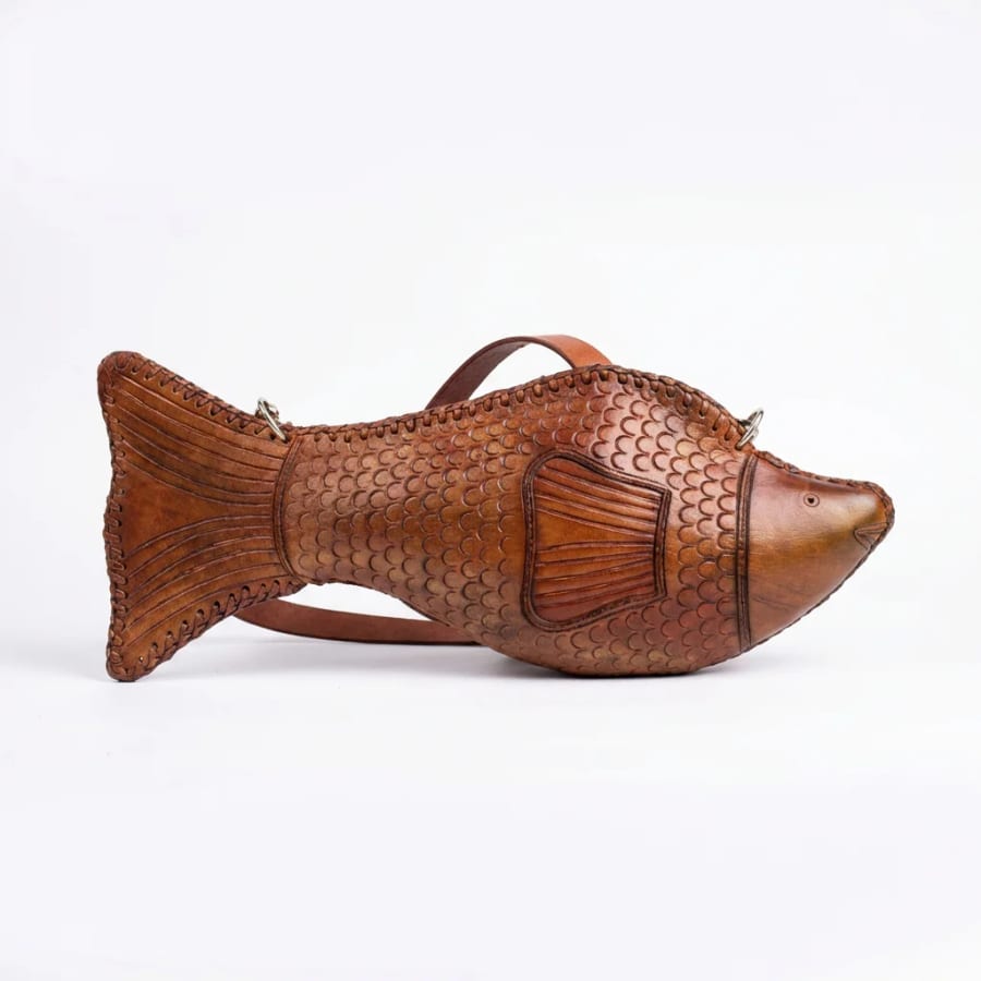 A medium tan leather fish bag with a broad tail and a shoulder strap, photographed on a plain pale background.