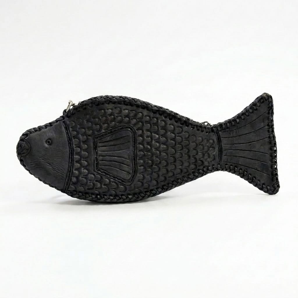 A black leather fish bag photographed alone on a plain pale background, seen from the side: punched scales across the body, a hand-laced edge, a broad tail and a zip along the back.