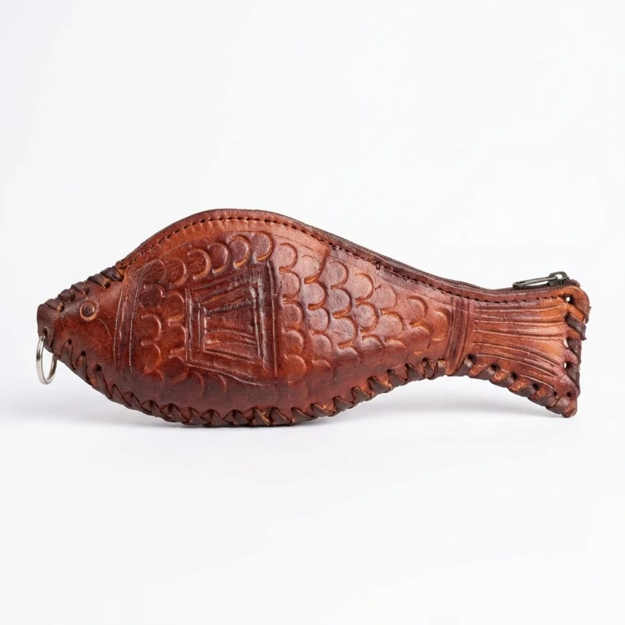 A small tan leather fish coin purse with a zip along the back, a hand-laced edge and a metal ring at the mouth, photographed alone on a plain pale background.
